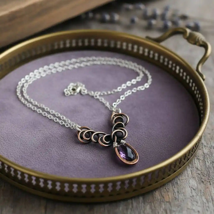 Silver and Copper Wire Sculpted Purple Crystal Drop Necklace displayed on a decorative tray with purple velvet.