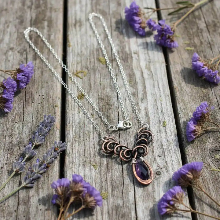 Silver and Copper Wire Sculpted Purple Crystal Drop Necklace displayed on wooden surface with flowers.