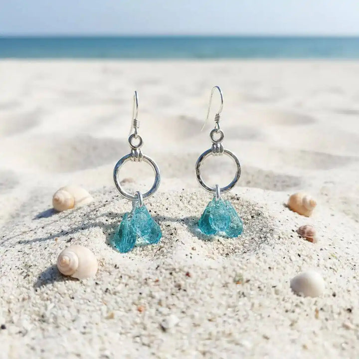925 Silver Hammered Aqua Crystal Cascading Drop Earrings on sandy beach with seashells, showcasing ocean-inspired elegance.