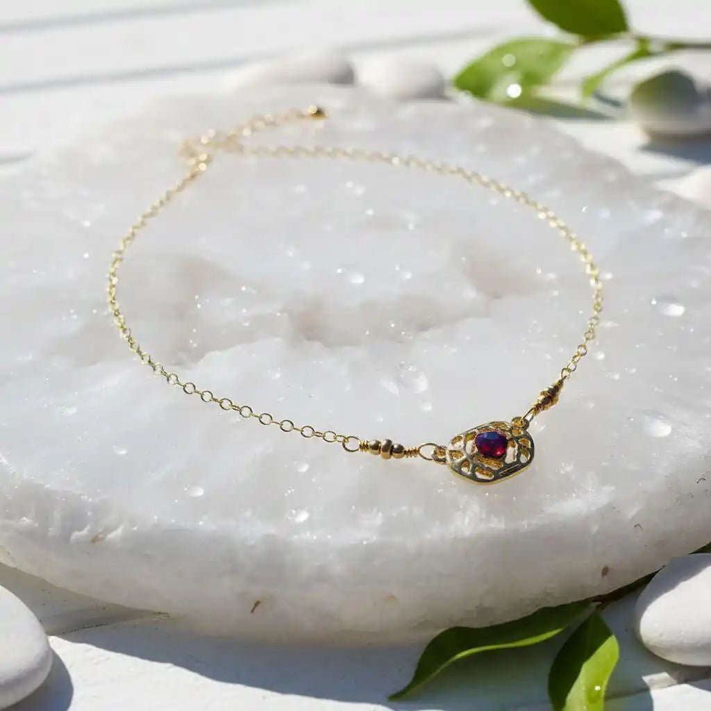 Red Crystal 14 K Gold Filled Adjustable Filigree Choker resting on a smooth white surface with greenery in the background.