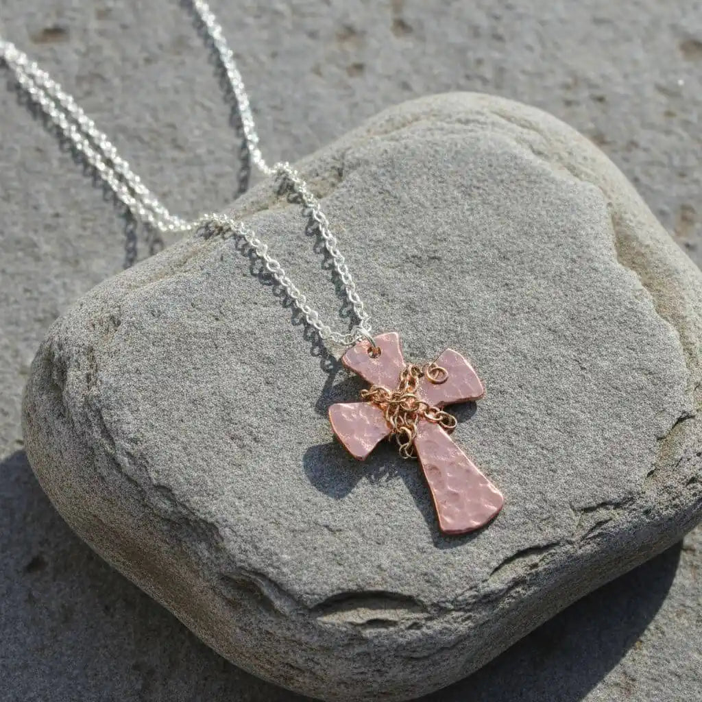 Chained Hammered Copper Cross Necklace For Him Or Her resting on a stone, showcasing its unique design and craftsmanship.