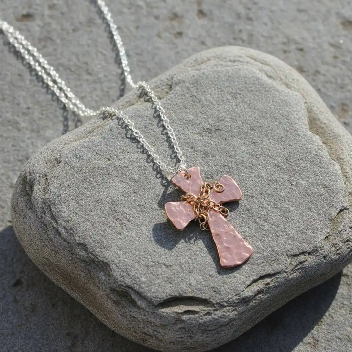 Chained Hammered Copper Cross Necklace For Him Or Her resting on a stone, showcasing its unique design and craftsmanship.