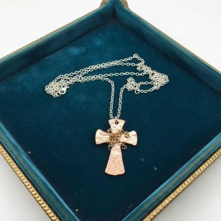 Chained Hammered Copper Cross Necklace For Him Or Her displayed on a blue velvet cushion.