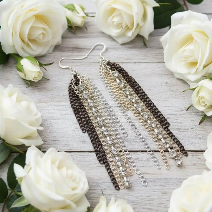 Rhinestone Crystal Chain Fringe Earrings displayed among white roses on a wooden surface.