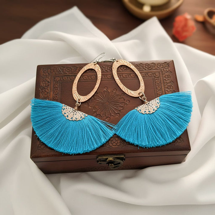 Long Copper Embossed Aqua Brushed Silk Fan Tassel Earrings displayed on a wooden box with white fabric.
