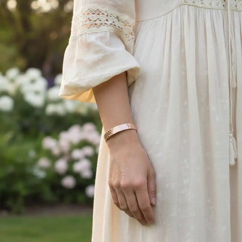 His and Her Copper Embossed Weave Cuffs 16 Gauge worn by a woman in a garden, showcasing artisan-crafted jewelry.