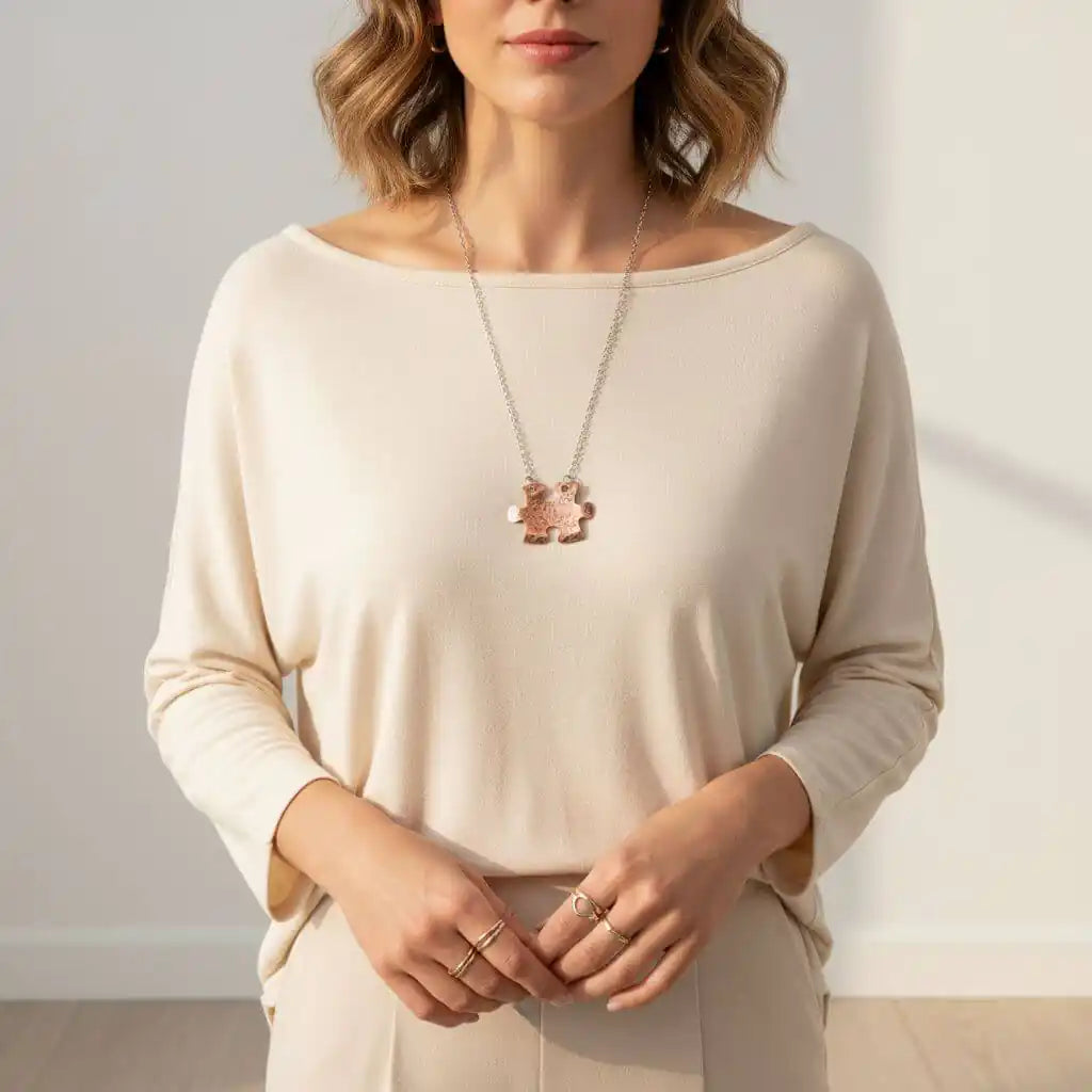 Woman wearing a beige long-sleeve top with a necklace and rings against a neutral background