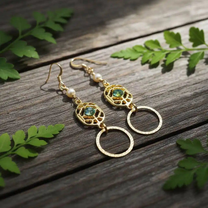 14 KT Gold Filled Green Crystal Circle Filigree Earrings displayed on wooden surface with green leaves.