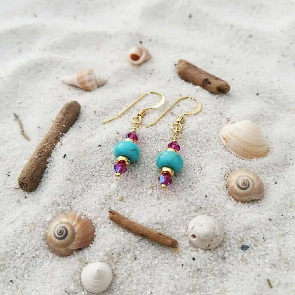 Hot Pink and Turquoise Gemstone14 K Gold Filled Earrings resting on sandy beach with seashells and driftwood