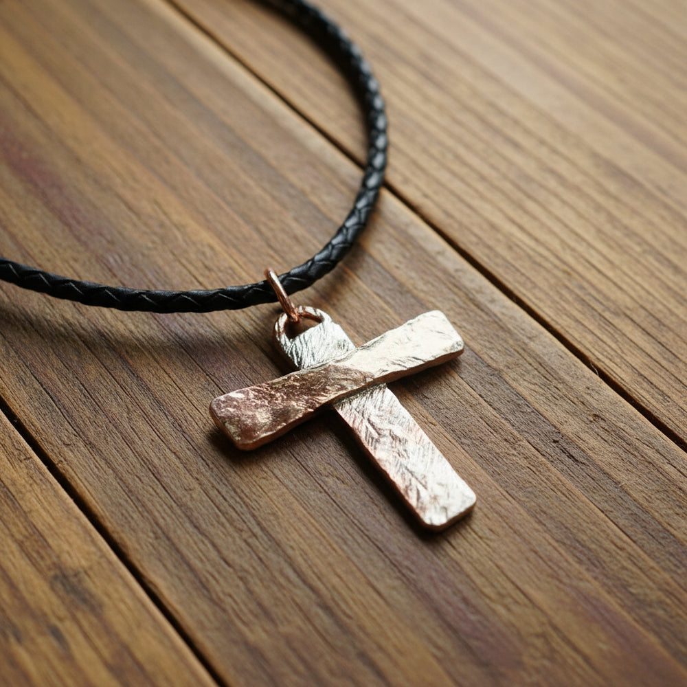 copper and silver cross pendant on a black leather cord against a rustic wooden table