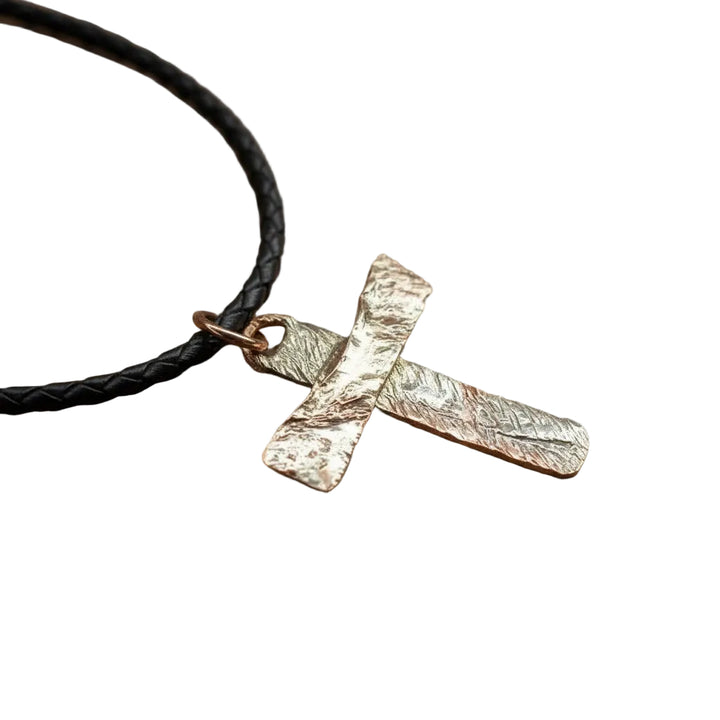 Gold cross pendant on a black cord against a gray background