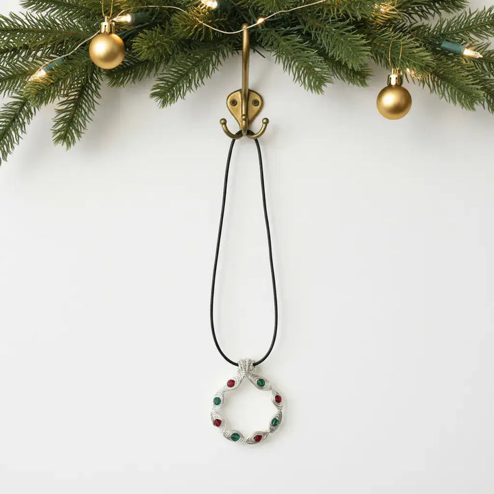 Christmas wreath necklace hanging on brass hook with garland