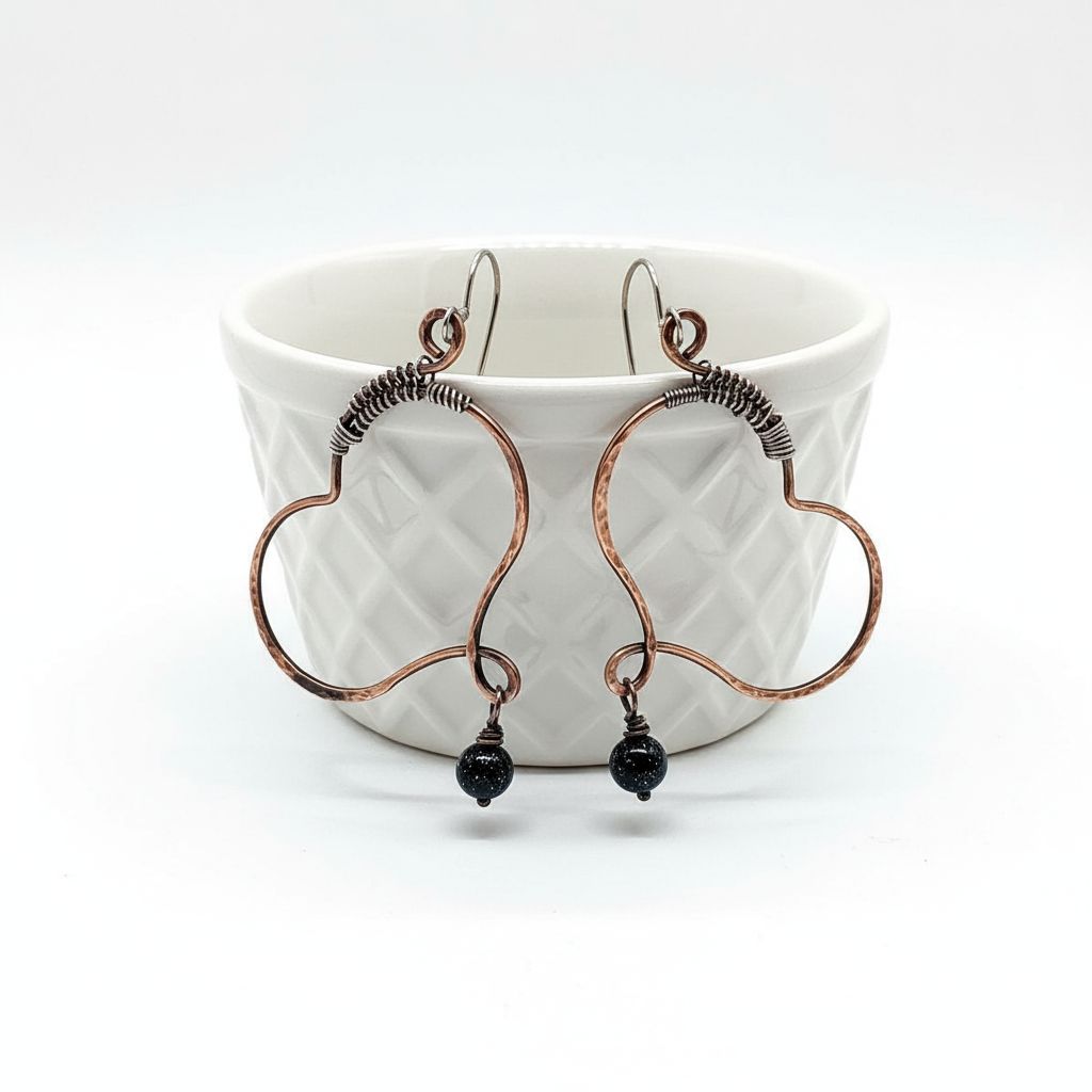 Sculpted Copper Butterfly Wing Abuse Survivor Earrings hanging from a bowl with black Swarovski crystal dangles.