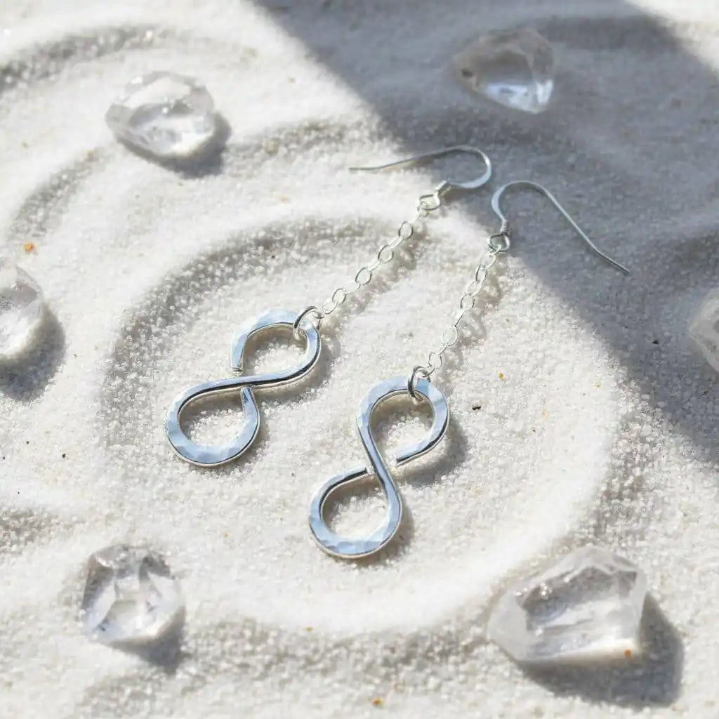Sterling Silver Hammer Patterned Infinity Earrings displayed on sandy background with crystals.