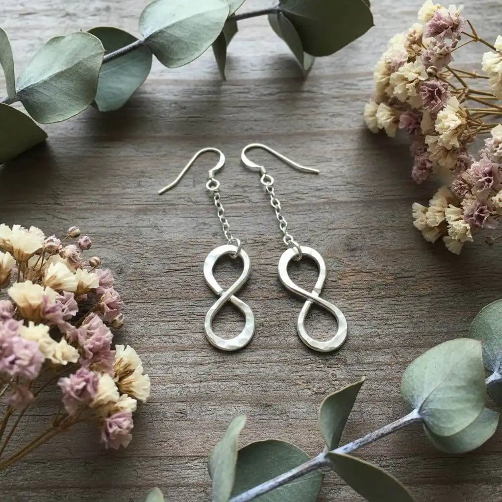 Sterling Silver Hammer Patterned Infinity Earrings displayed with flowers and foliage on rustic wood.