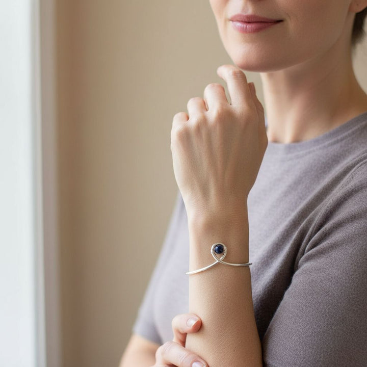 Silver Blue Bead Child Abuse Awareness Ribbon Bangle worn on a woman's wrist, showcasing the blue sandstone bead.