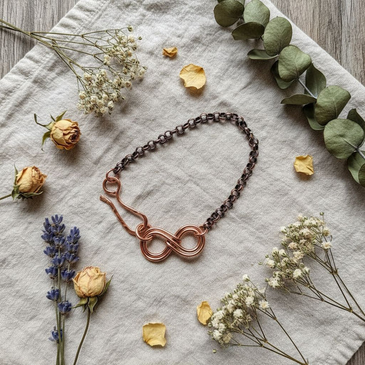 Wire Sculpted Copper Double Infinity Chain Bracelet displayed on a soft fabric with dried flowers.