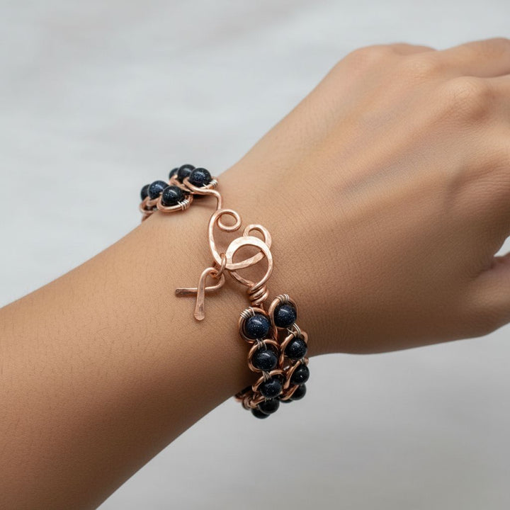 Wire Sculpted Blue Beaded Infinity Child Abuse Bangle worn on wrist, featuring copper and blue sandstone beads.