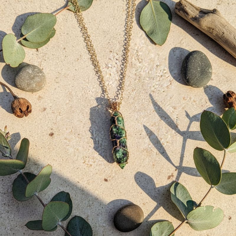 Gold Wire Caged In Ruby In Zoisite Pointed Crystal Necklace displayed among natural elements and stones