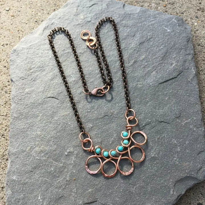 Seen on Ashley Liao Copper Turquoise Wire Wrapped Necklace on a stone surface, featuring circular designs and turquoise beads.