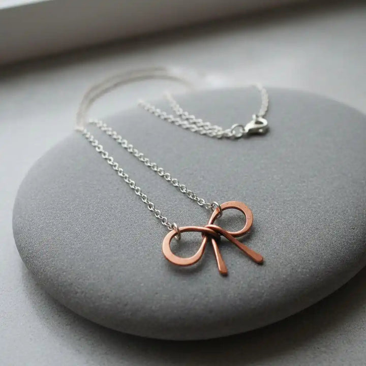 Wire Wrapped Copper Bow Tie Silver Chain Necklace on smooth grey stone background.