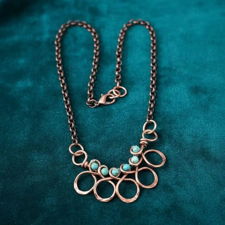 Seen on Ashley Liao Copper Turquoise Wire Wrapped Necklace on a teal background.