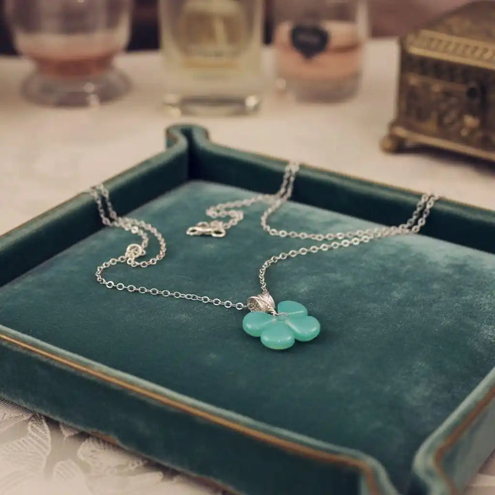 Mint green beaded clover necklace displayed on a velvet tray with elegant decor in the background.