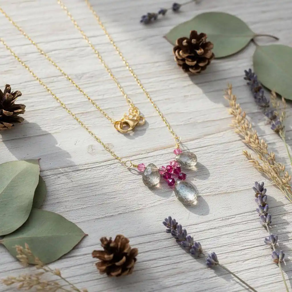 Adjustable Gold Filled Wire Wrapped Gemstone Necklace featuring rainbow quartz and fuchsia Swarovski crystals on a wooden background.