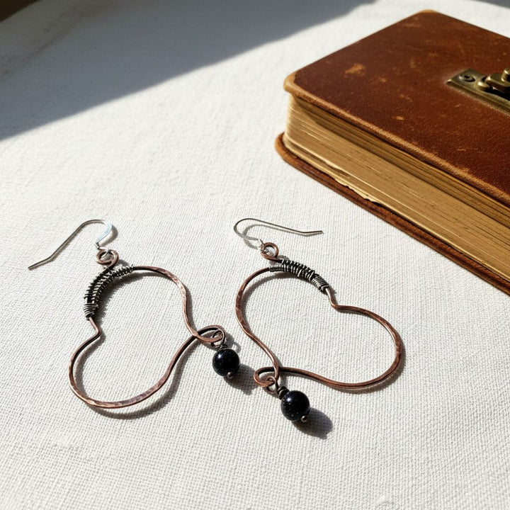 Sculpted Copper Butterfly Wing Abuse Survivor Earrings with black Swarovski crystal dangles on a bright background.