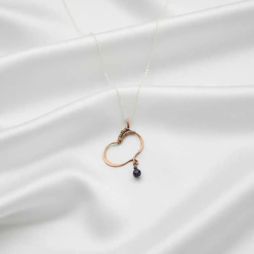 Hammered Copper Butterfly Wing Child Abuse Survivor Necklace with purple crystal pendant on a satin background.