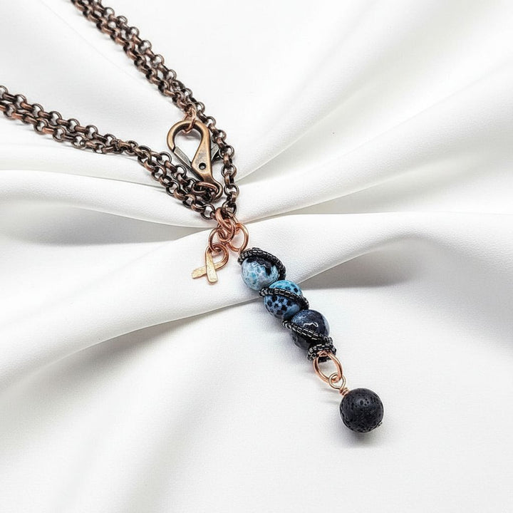 Child Abuse Awareness Agate Necklace With Lava Rock Bead featuring blue agate beads and lava rock charm on a copper chain.