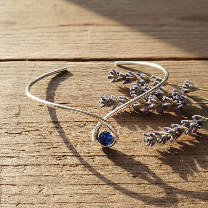 Silver Blue Bead Child Abuse Awareness Ribbon Bangle on wooden surface with lavender flowers.