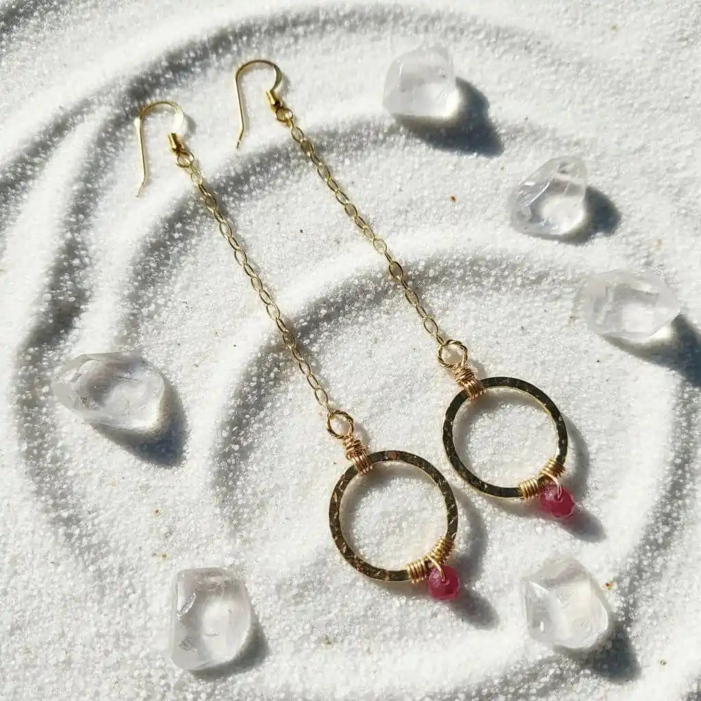 Gold Filled Wrapped Pink Chalcedony Open Circle Earrings with pink chalcedony stones on a sandy background.
