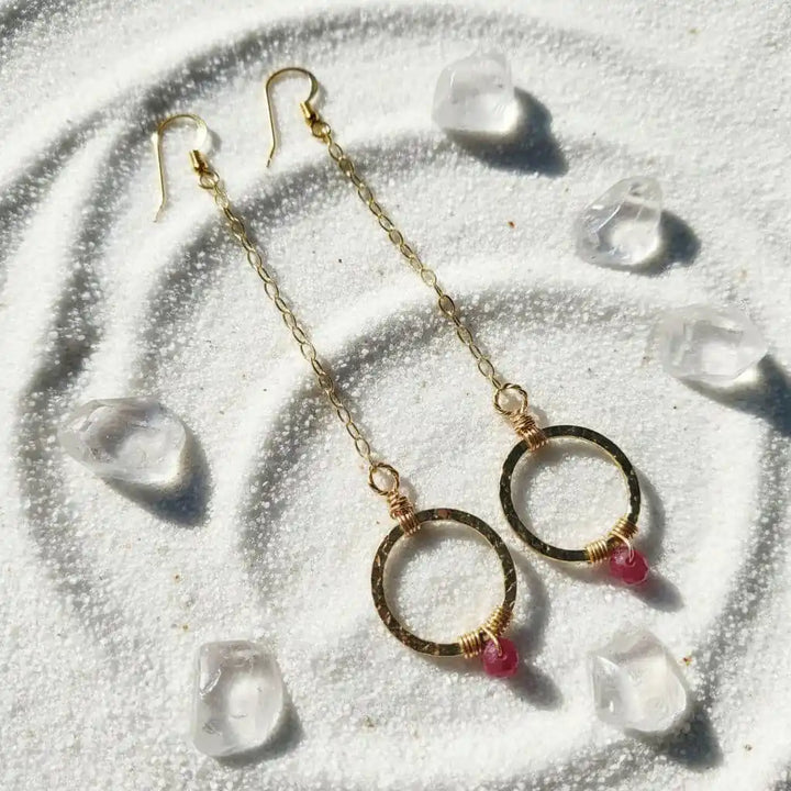 Gold Filled Wrapped Pink Chalcedony Open Circle Earrings with pink chalcedony stones on a sandy background.