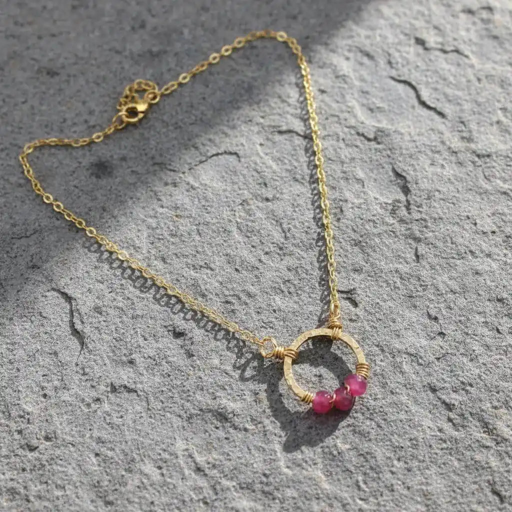 Gold Filled Pink Chalcedony Open Circle Necklace with gold chain and pink chalcedony beads on a textured stone surface.