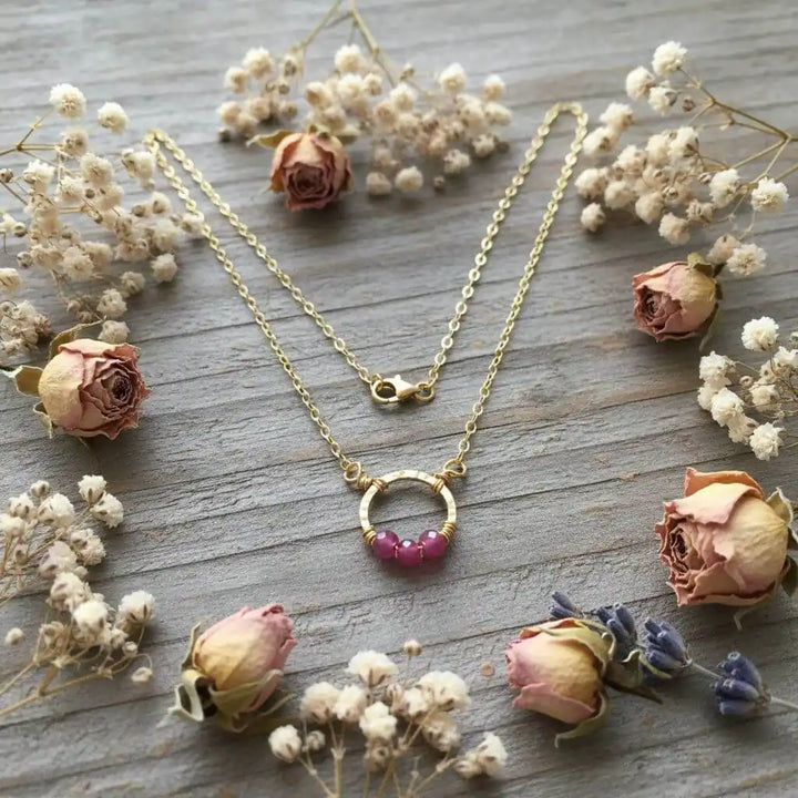 Gold Filled Pink Chalcedony Open Circle Necklace surrounded by dried roses and flowers.