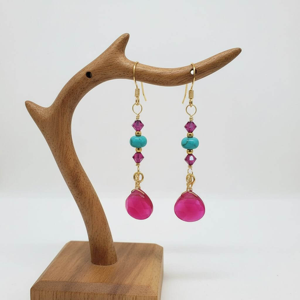 Gold Filled Wire Wrapped Pink Turquoise Gemstone Earrings displayed on a wooden earring stand with pink and turquoise beads.