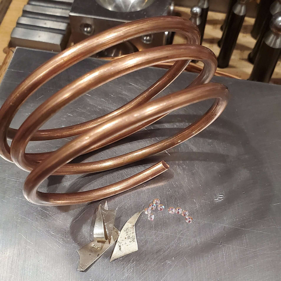 picture of 4 gauge raw solid copper coil besides sterling silver scrap pieces and flat swarovki crystals placed on stainless steel anvil.