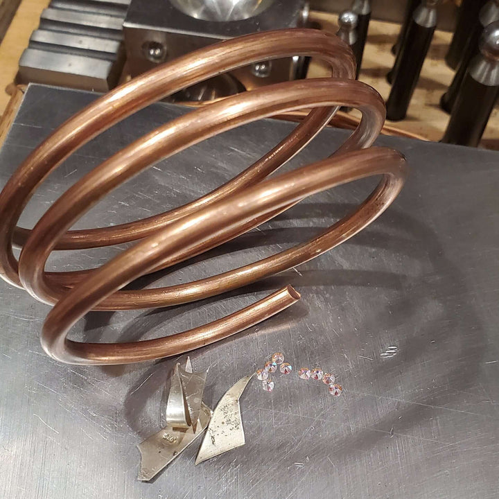 picture of 4 gauge raw solid copper coil besides sterling silver scrap pieces and flat swarovki crystals placed on stainless steel anvil.