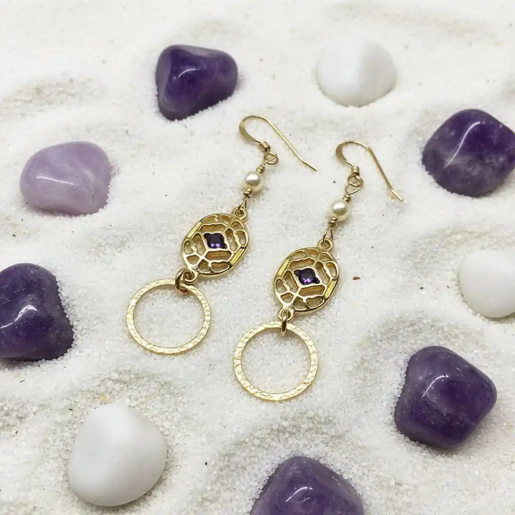 14 K Gold Filled Purple Crystal Circle Filigree Earrings with pearls on a sandy surface.